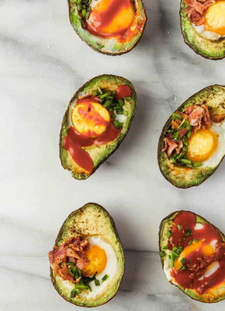 baked eggs in avocado whole30 breakfast on a marble board with hot sauce