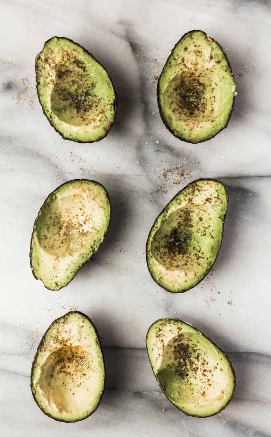 avocados on a marble board with the pits scooped out seasoned with salt and pepper