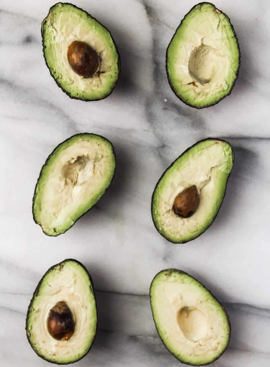 avocados sliced in half with pits removed on a marble board is the first step in this easy whole30 breakfast idea