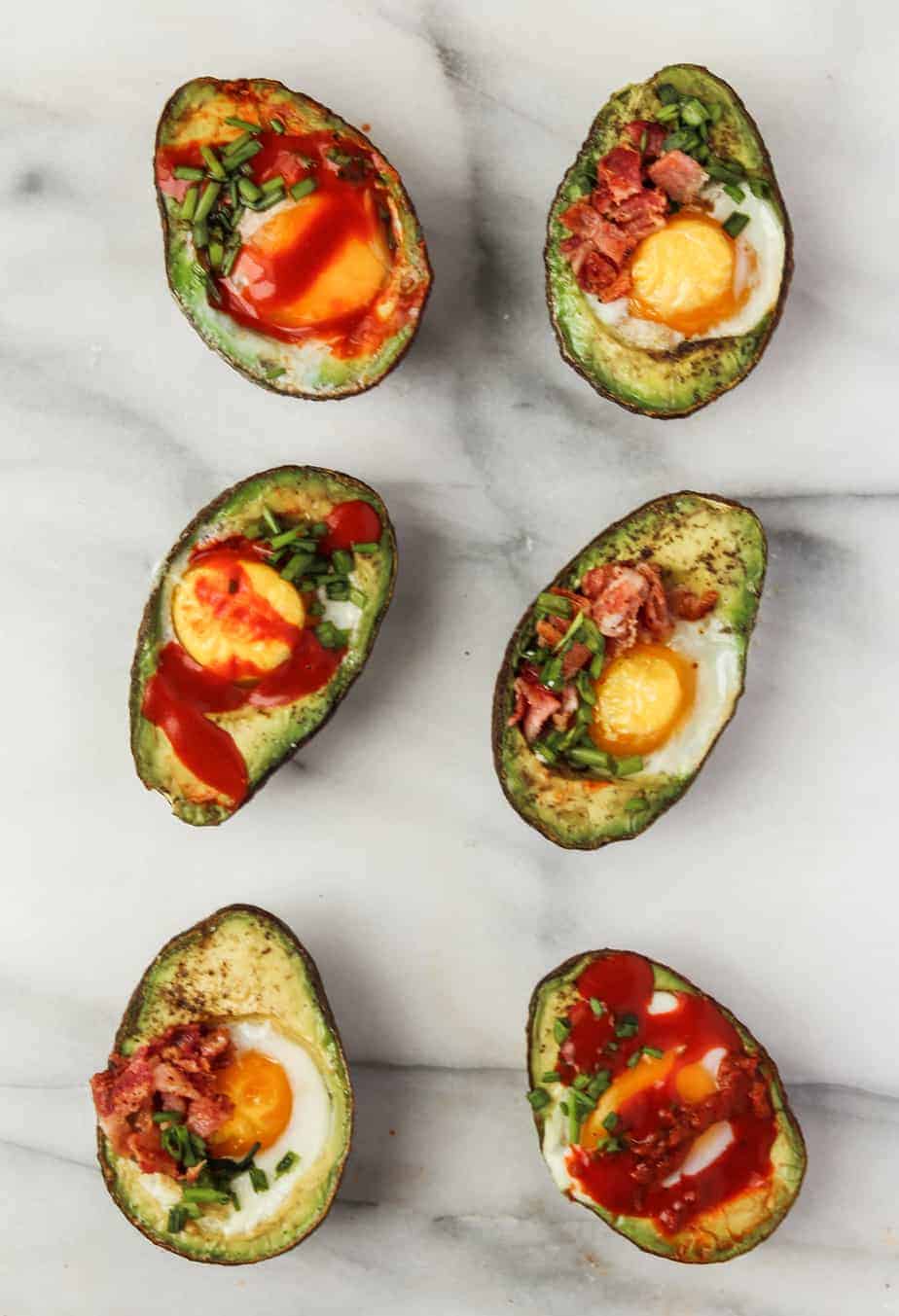 eggs and avocado breakfast recipe with hot sauce, chives and bacon on a marble platter 