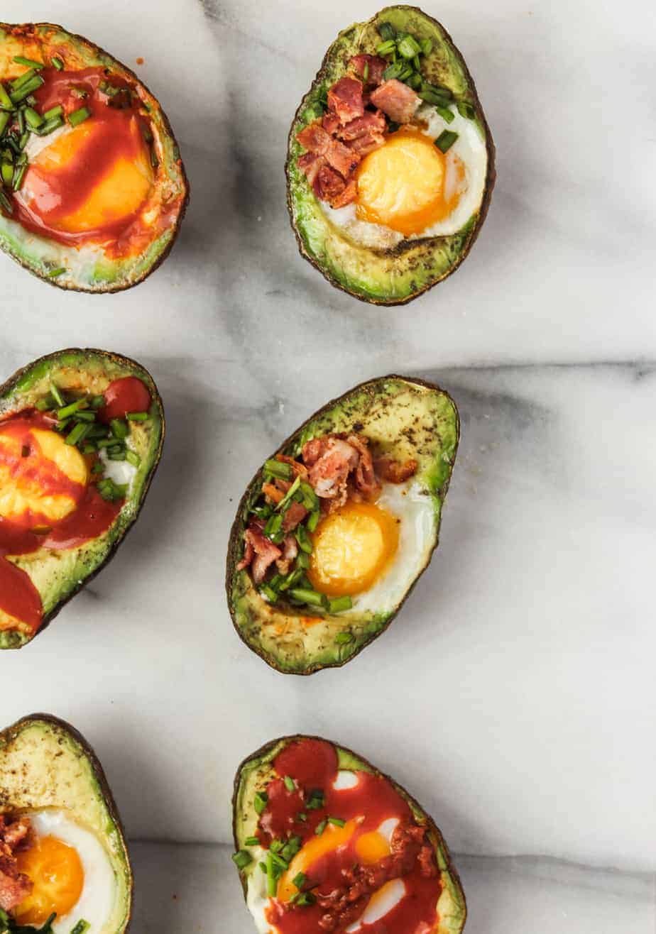 baked eggs in avocados on a marble platter with bacon, chives and hot sauce is an easy whole30 breakfast idea