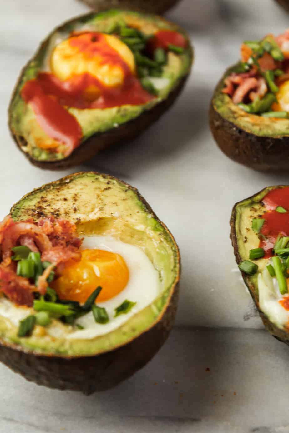 close up shot of baked eggs in avocados topped with bacon, chives and hot sauce