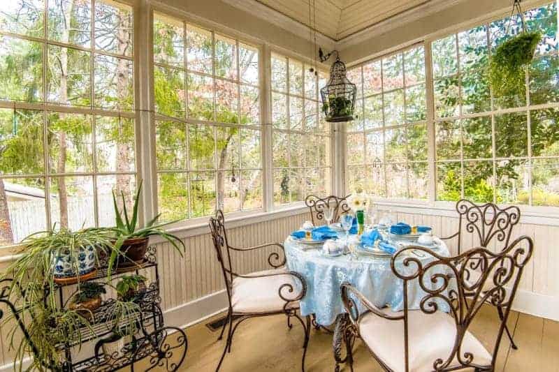 a dining table with a blue table cloth and blue napkins with four chairs in a room full of windows and a plant cart at an asheville b&b