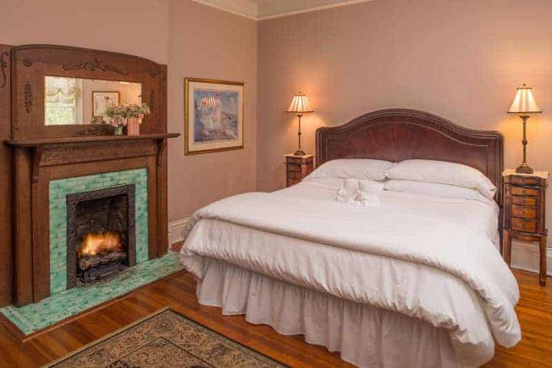 wooden bed with white linens and a wood and green tiled fireplace at an asheville bed and breakfast