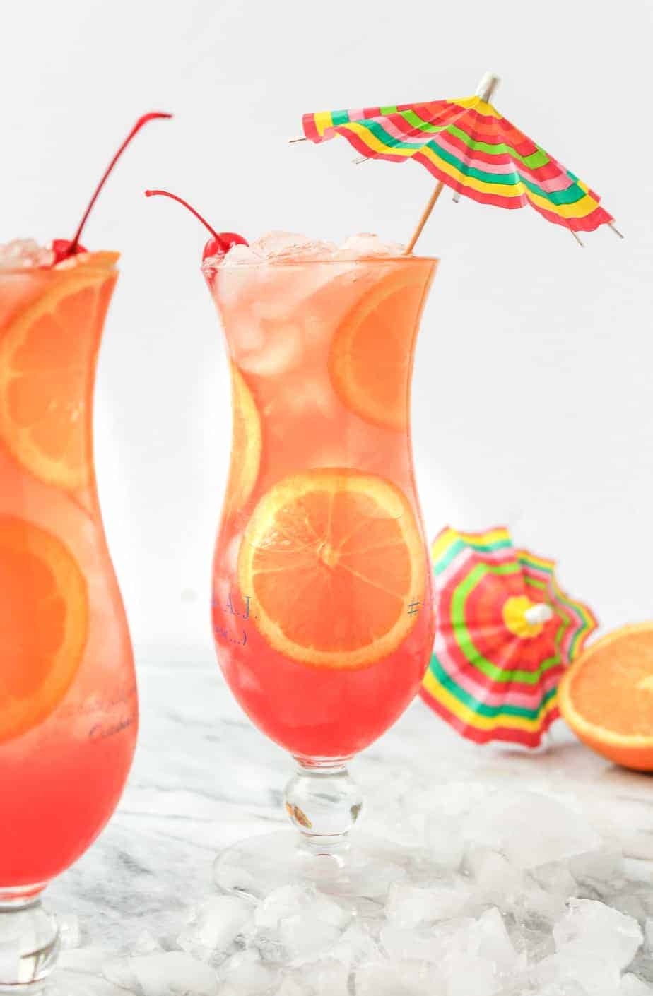 hurricane drink in a hurricane glass with an orange slice and garnished with a cherry and umbrella