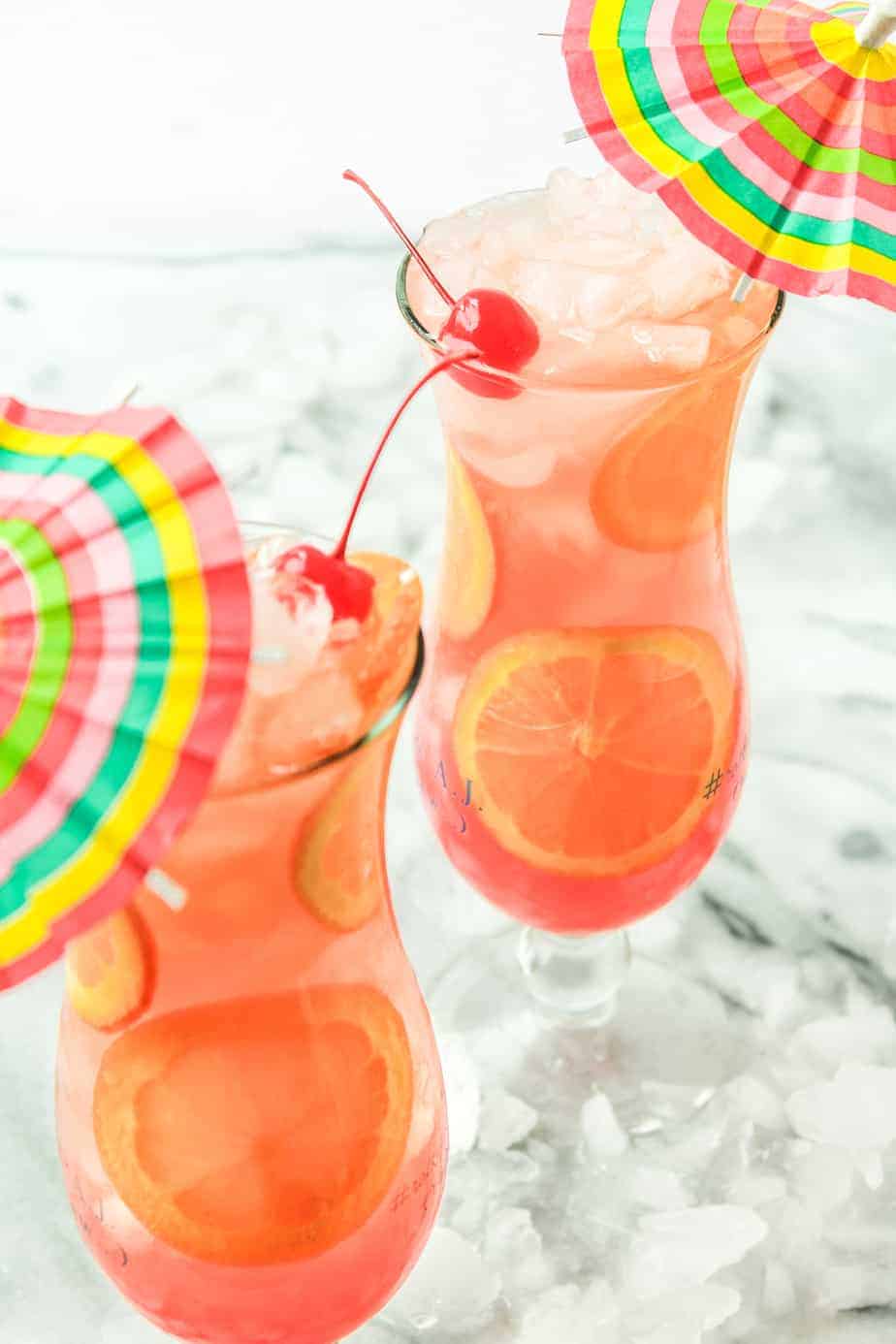 two mardi gras cocktails with orange slices and cherries in hurricane glasses