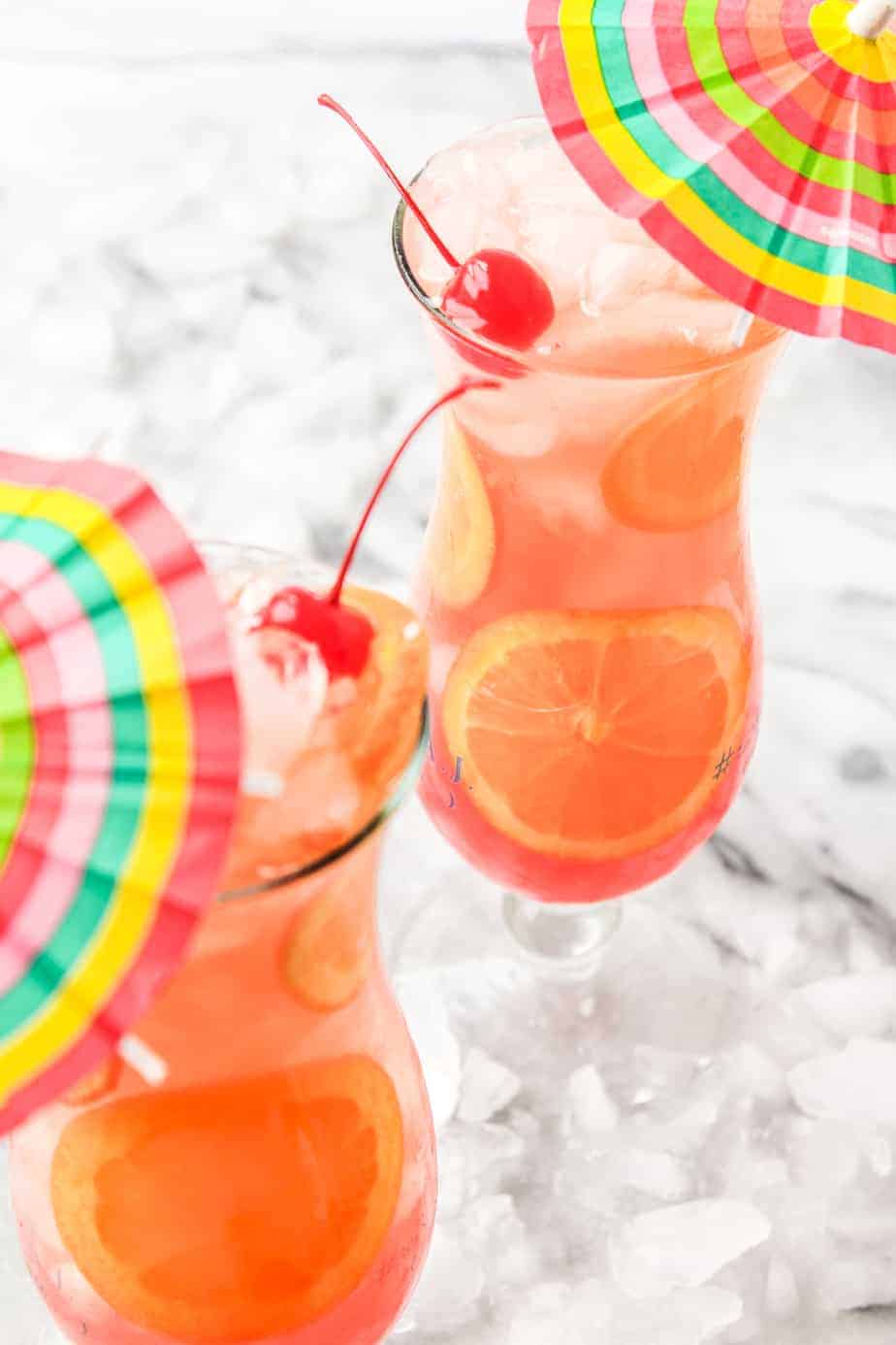 two hurricane cocktails with orange slices and cherries in hurricane glasses