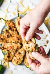 eating a crab stuffed baked jalapeno popper with white plate of poppers