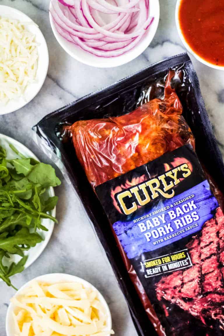 curly's ribs with other ingredients needed like arugula, cheese, red onion and bbq sauce for a grilled bbq pizza on a marble board