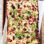 grilled bbq pizza on parchment paper and a baking sheet pan with ribs, red onion, gouda cheese and arugula