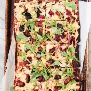 grilled bbq pizza on parchment paper and a baking sheet pan with ribs, red onion, gouda cheese and arugula