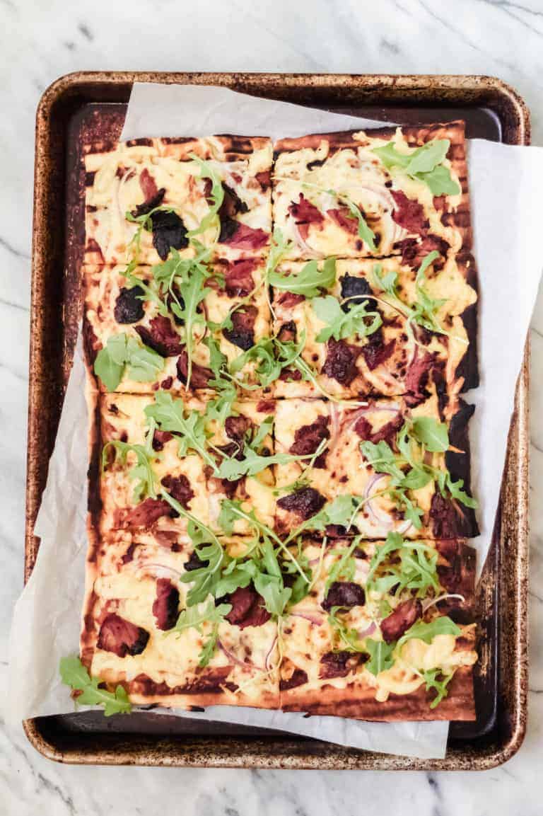 grilled bbq pizza on parchment paper and a baking sheet pan with ribs, red onion, gouda cheese and arugula