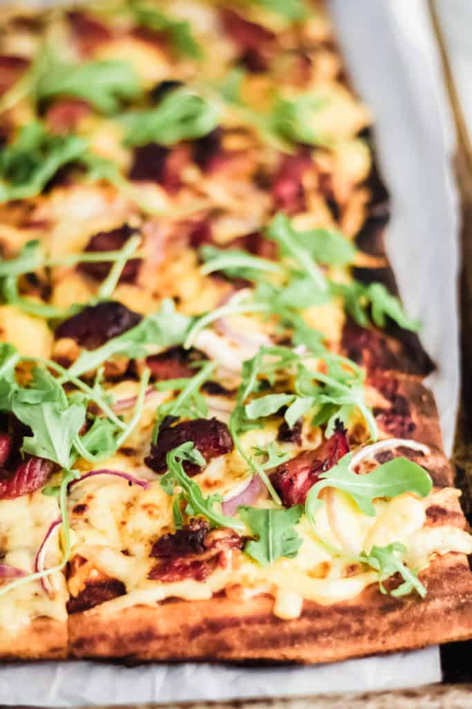 corner of a square grilled pizza with bbq ribs on parchment paper