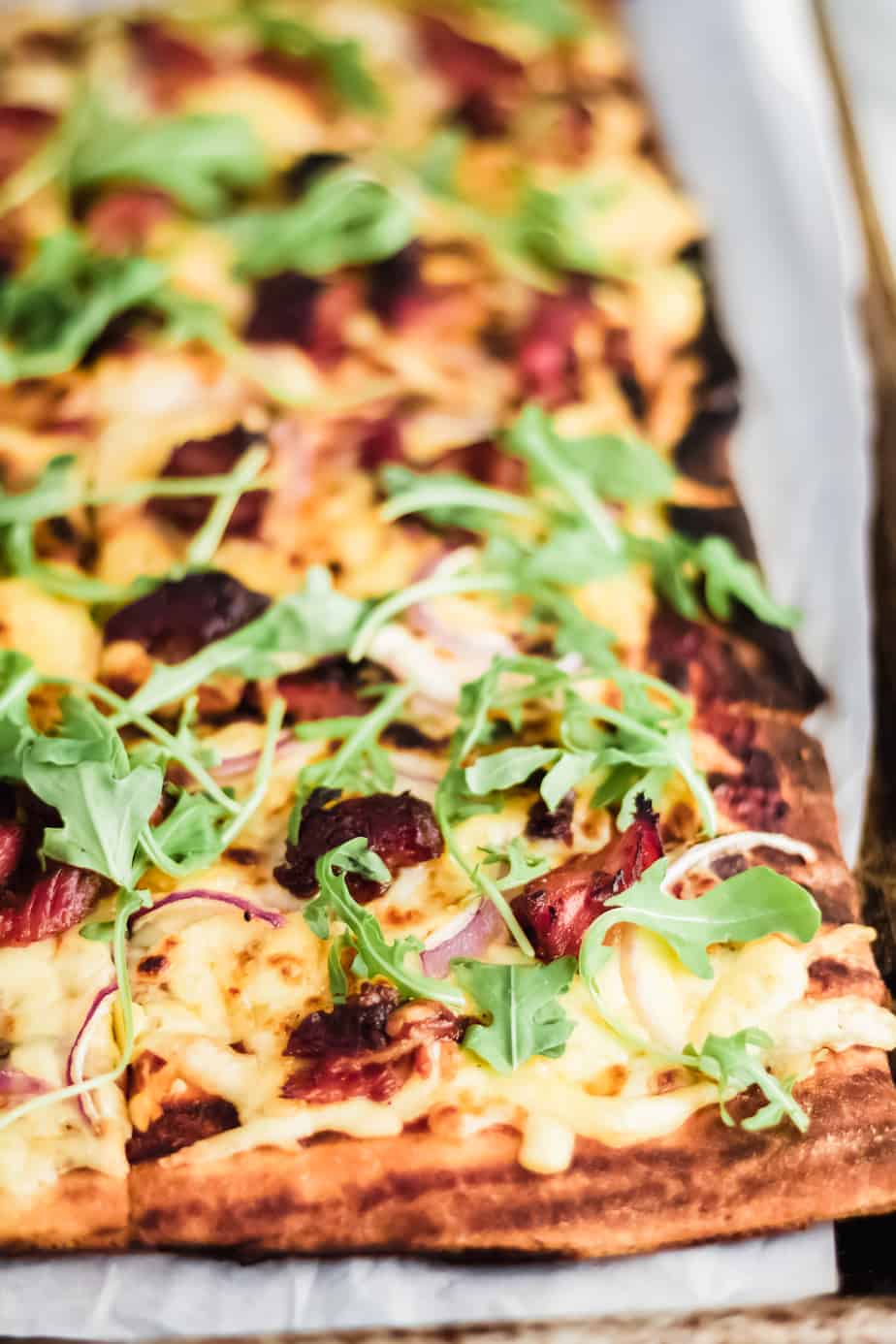 corner of a square grilled pizza with bbq ribs on parchment paper