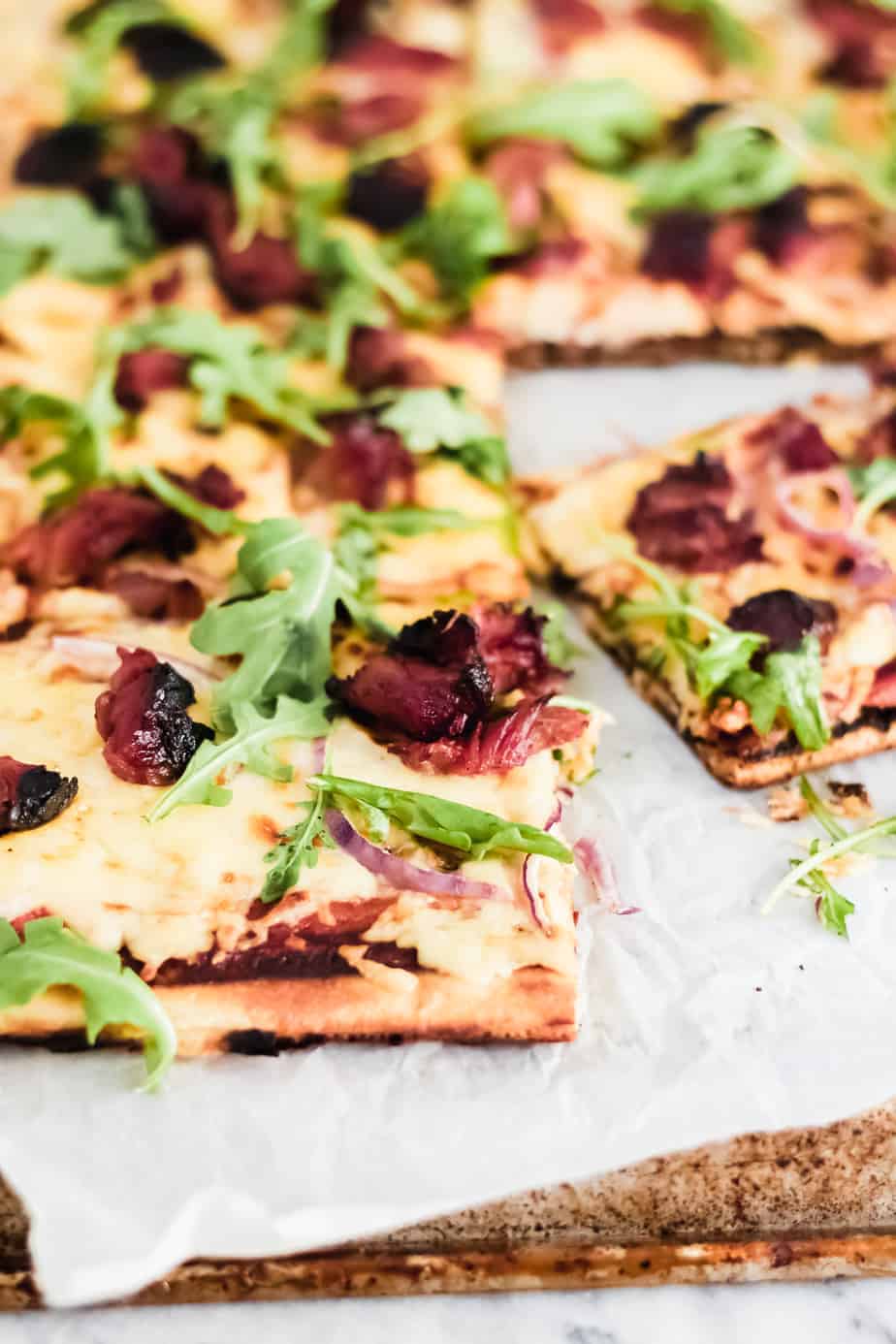 slice of grilled bbq pizza on parchment paper with arugula and bbq ribs