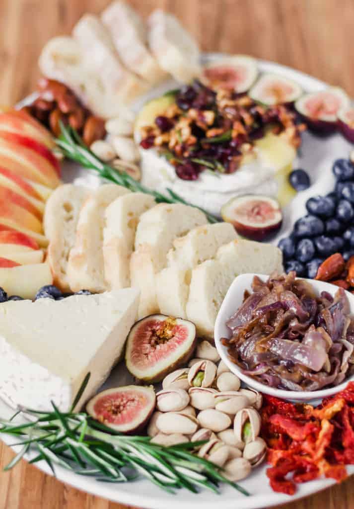 cheese board on a white platter and a wooden surface with fruit and brie