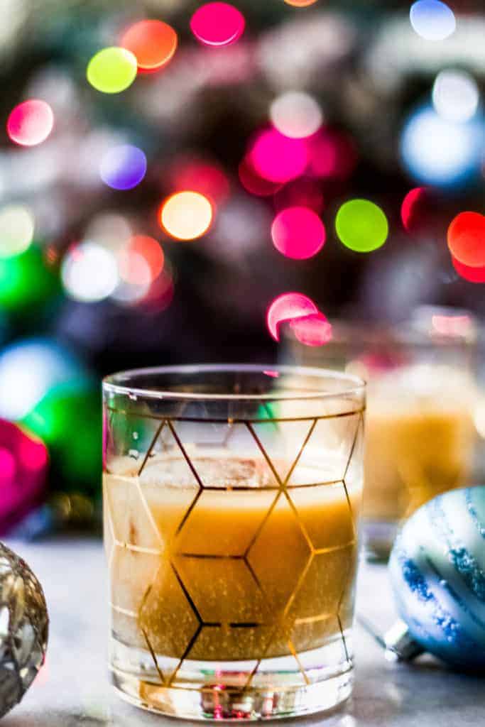 two eggnog white russian cocktails in front of a christmas tree with multi colored lights