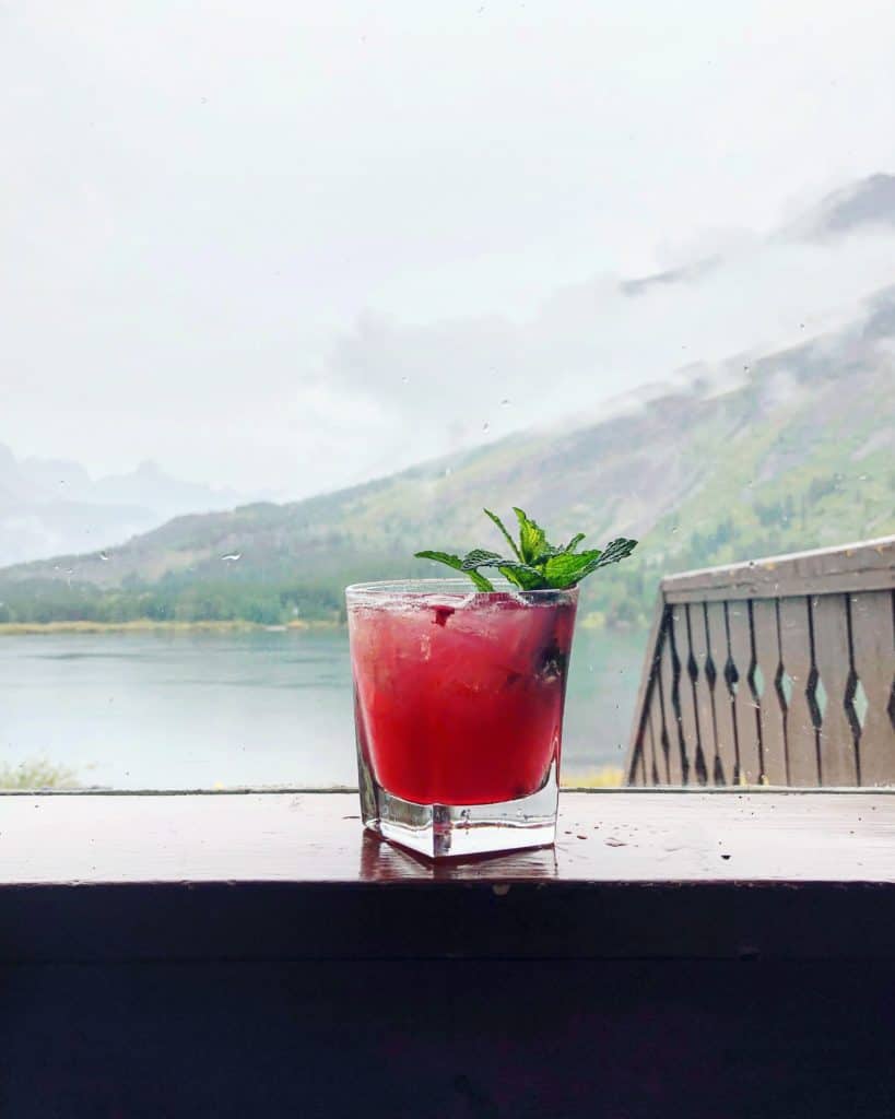 huckleberry smash cocktail on a window ledge with mountains in the background