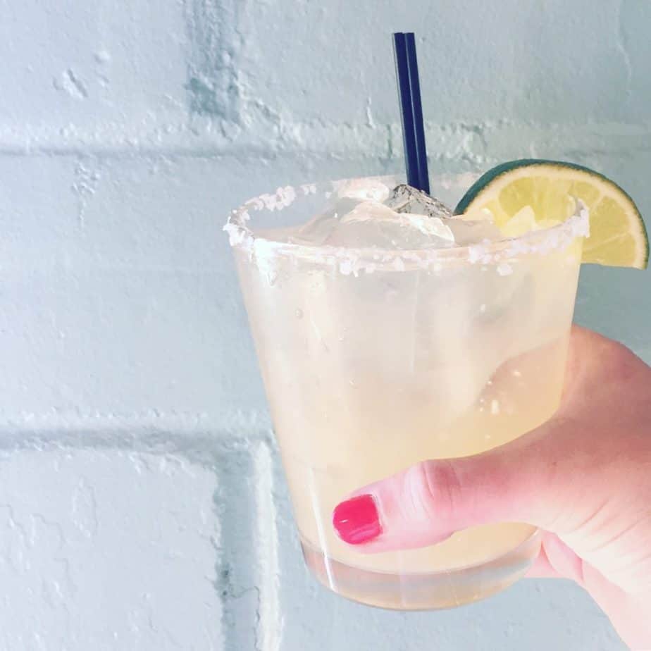 margarita being held up with fresh lime in front of a green wall