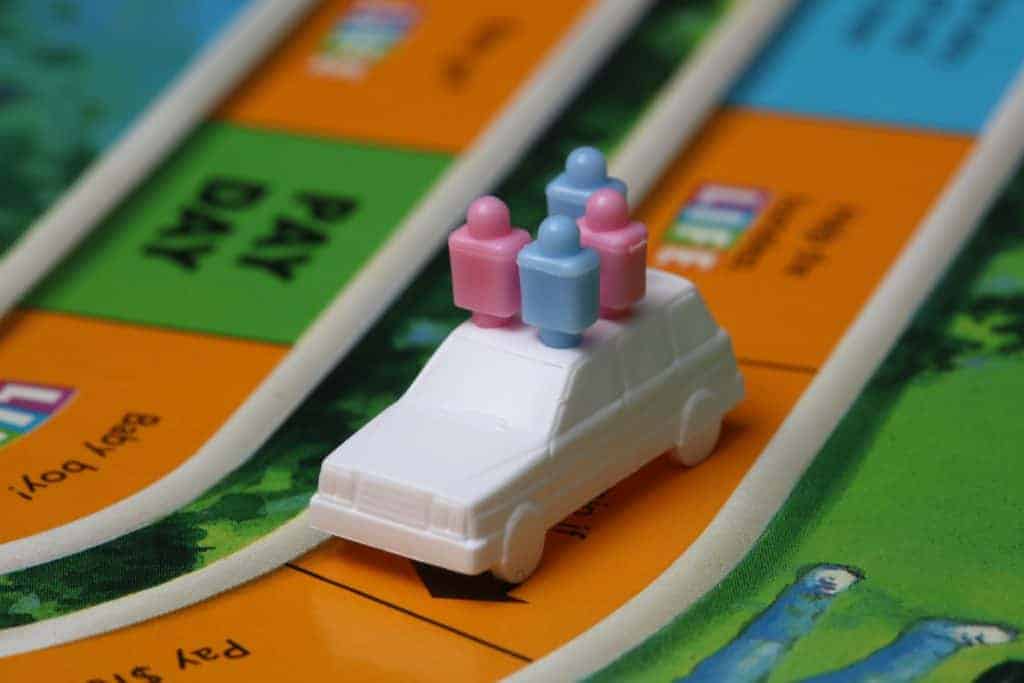 game of life board with two blue pieces and two pink pieces in a white car