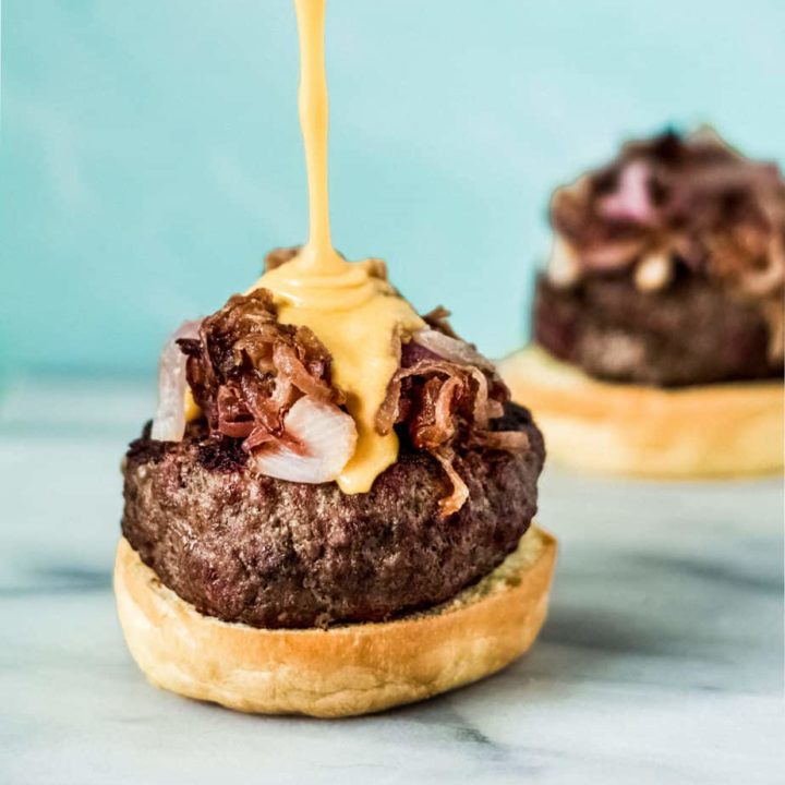 beer cheese sauce being poured on a burger