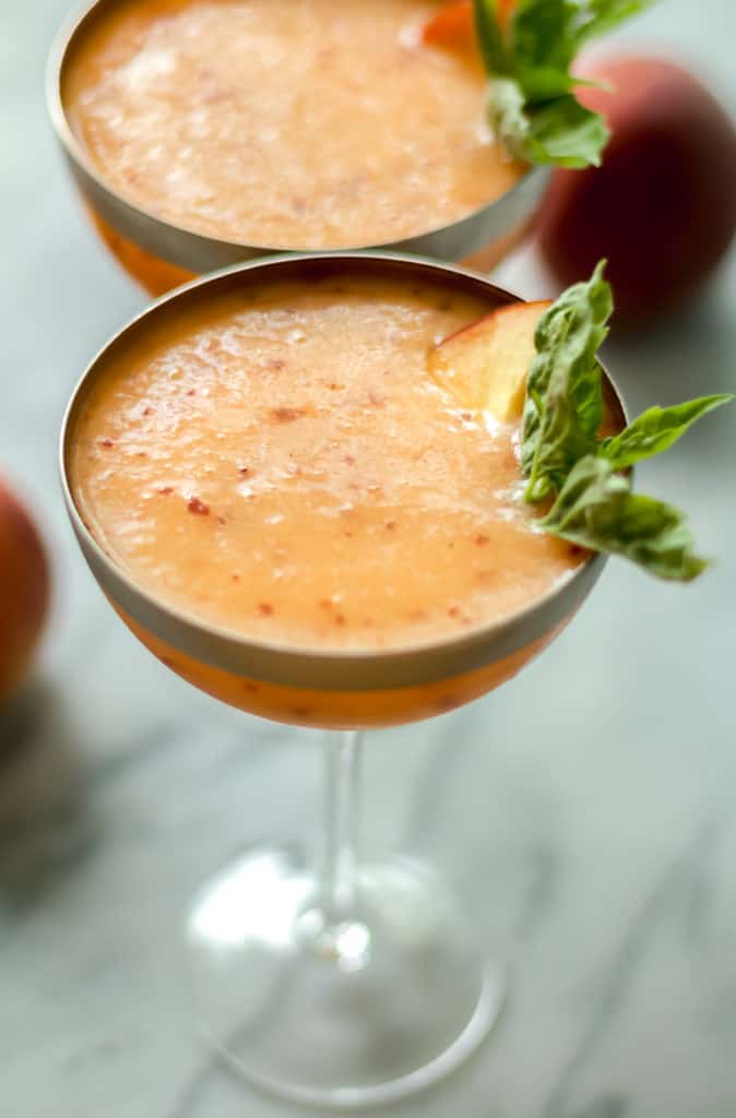 close up angle of peach frose in a cocktail glass garnished with basil