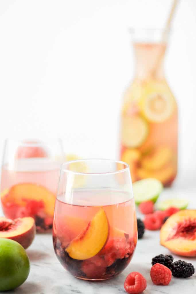 two glasses and a carafe of sparkling peach sangria with fresh fruit