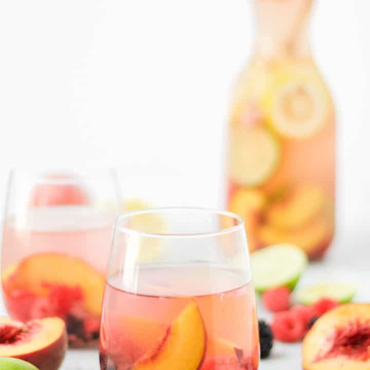 two glasses and a carafe of sparkling peach sangria with fresh fruit