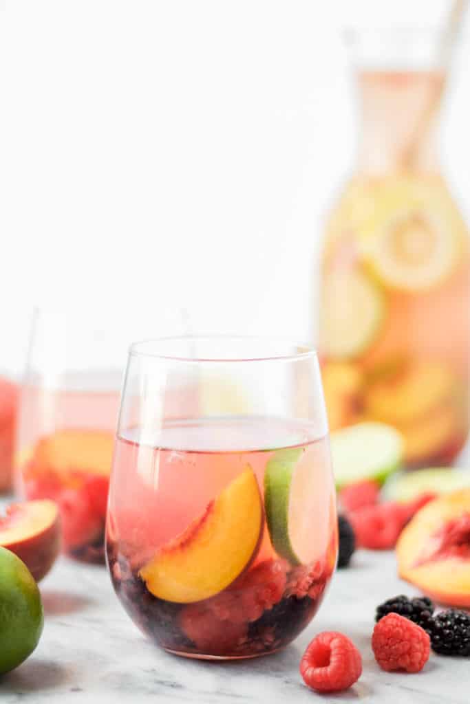 two glasses of sparkling peach sangria with slices of peaches, raspberries and blackberries