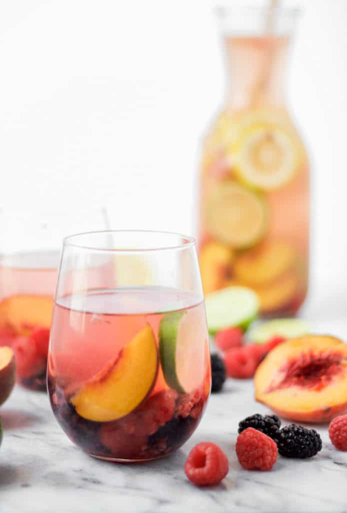 white wine sangria in a wine glass on a marble board with a peach half and raspberries