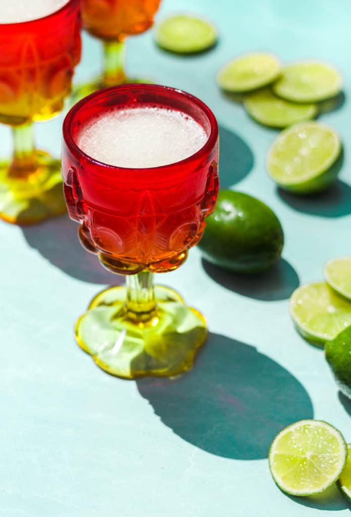 frozen gin and tonic in a red and white glass with a full lime and lime slices on a blue background