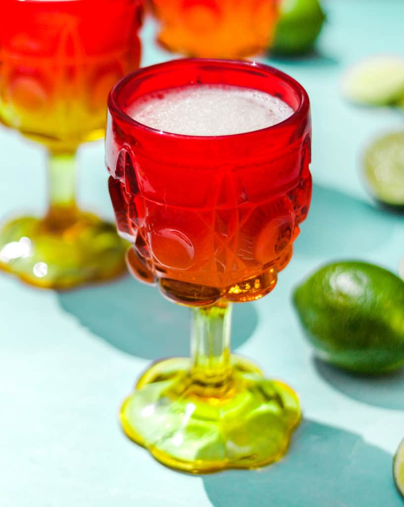 single frozen gin and tonic cocktail in a red and yellow glass with a lime next to it