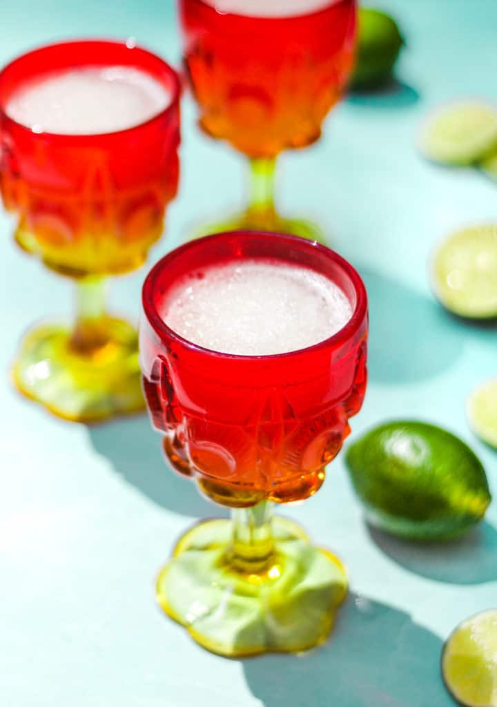 three red and yellow glasses of gin and tonic cocktails next to whole and sliced limes