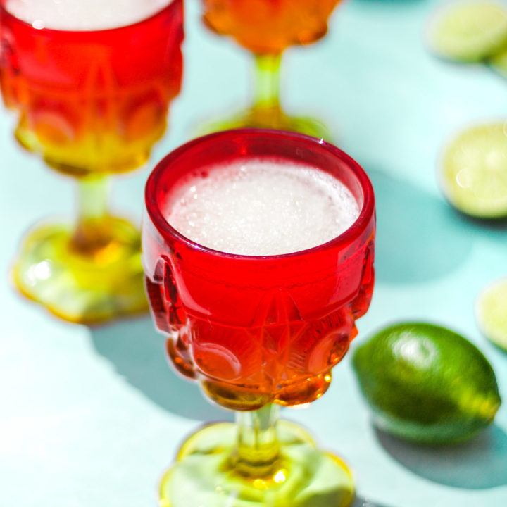 three red and yellow glasses of gin and tonic cocktails next to whole and sliced limes