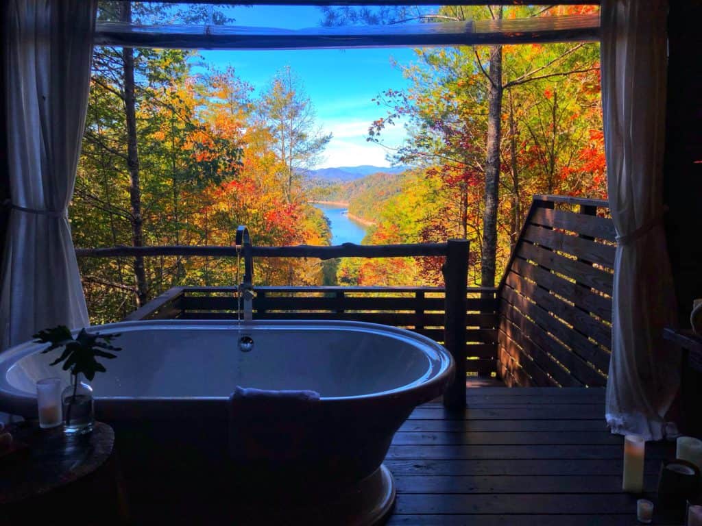 white tub on a wooden porch with colorful fall leaves and a lake in the background