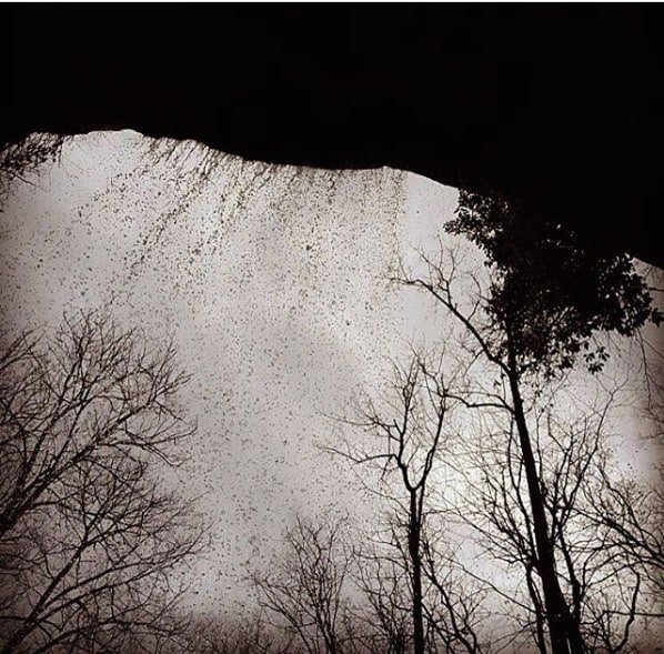 black and white photo underneath a rock behind a waterfall