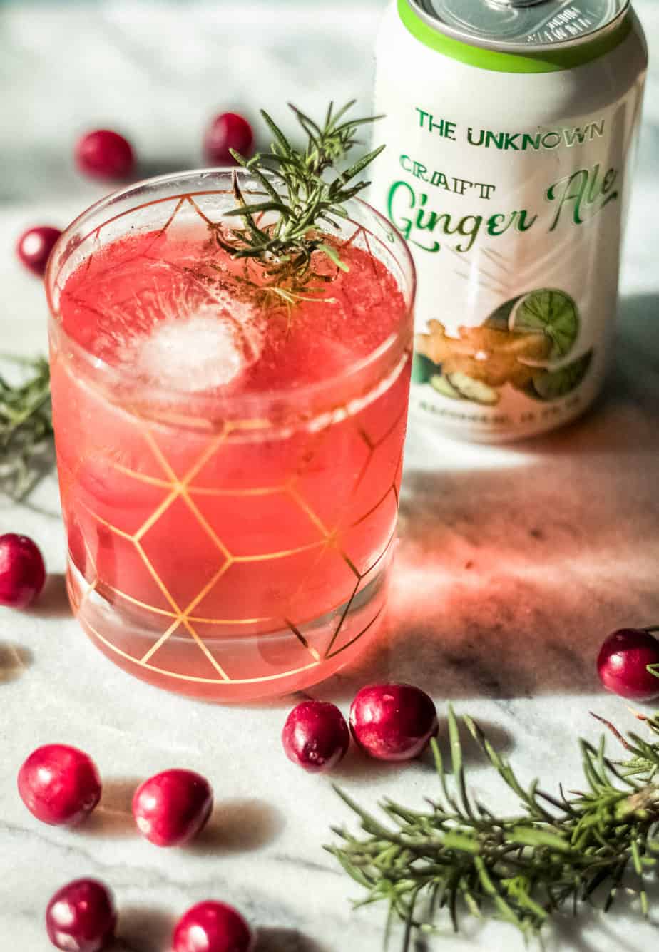 cranberry bourbon smash with can of ginger ale on a marble background with whold cranberries