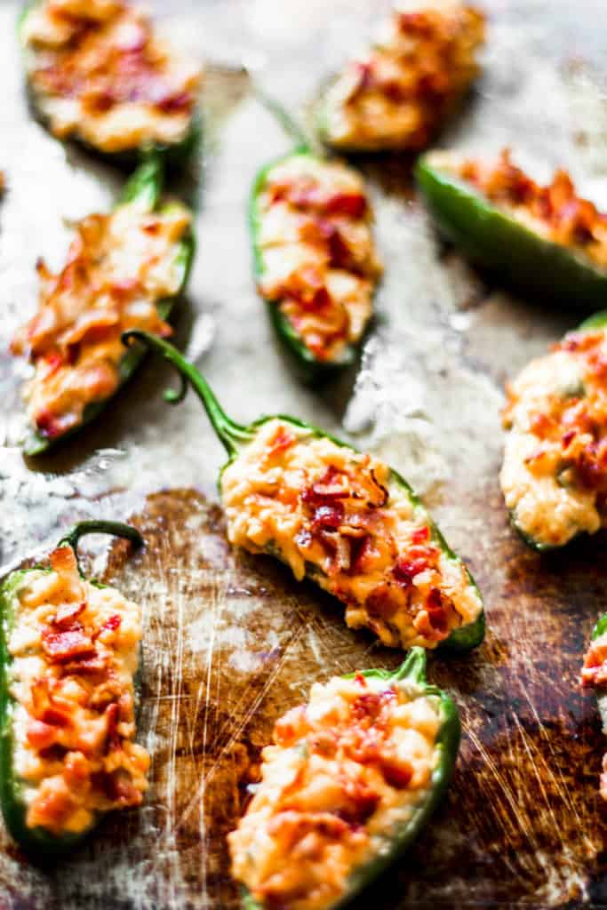 an assortment of jalapeno poppers with cheese and bacon on a metal sheet tray