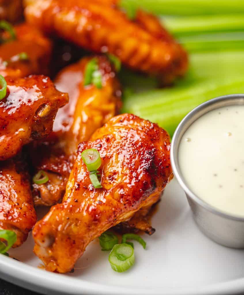 chicken wings on a while plate topped with green onions and a side of celery and ranch