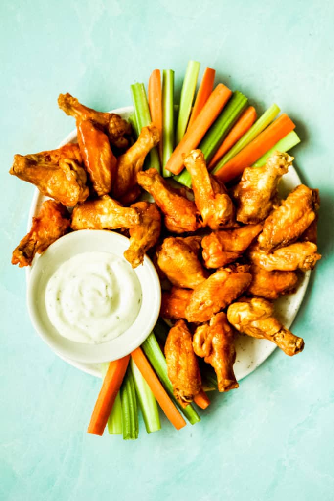 a plate of chicken wings with carrot and celery sticks and ranch sauce with a blue background