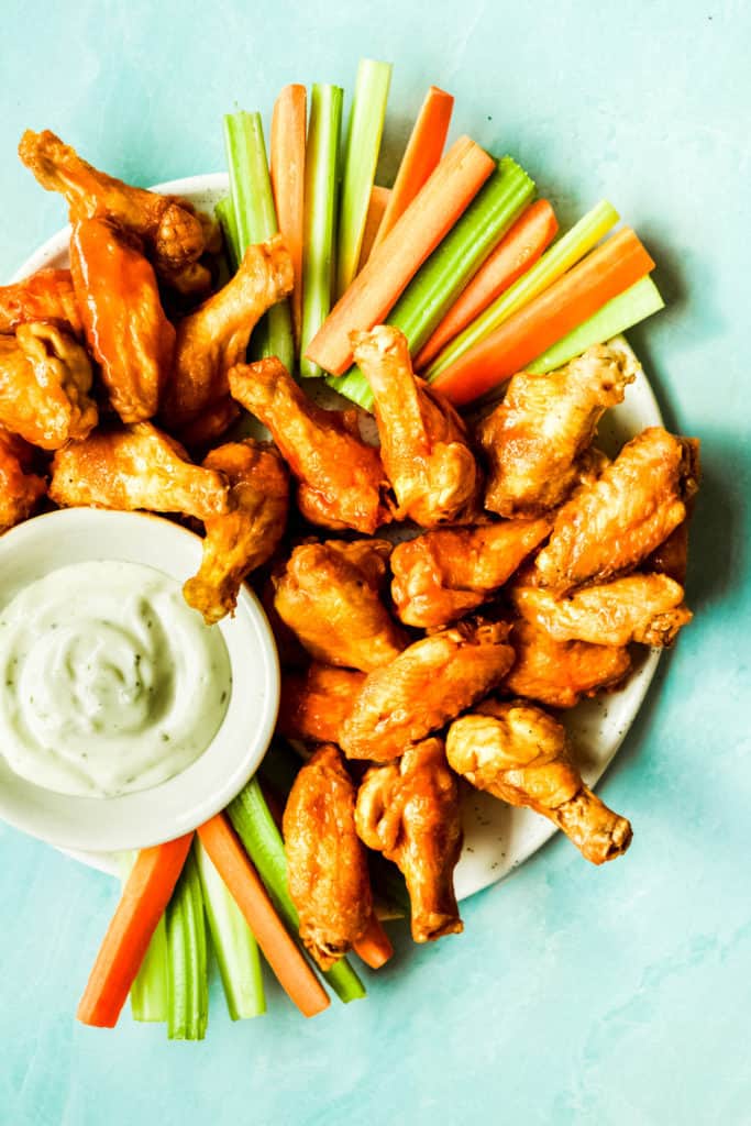 buffalo wings piled high on a plate with carrot and celery sticks and a bowl of ranch