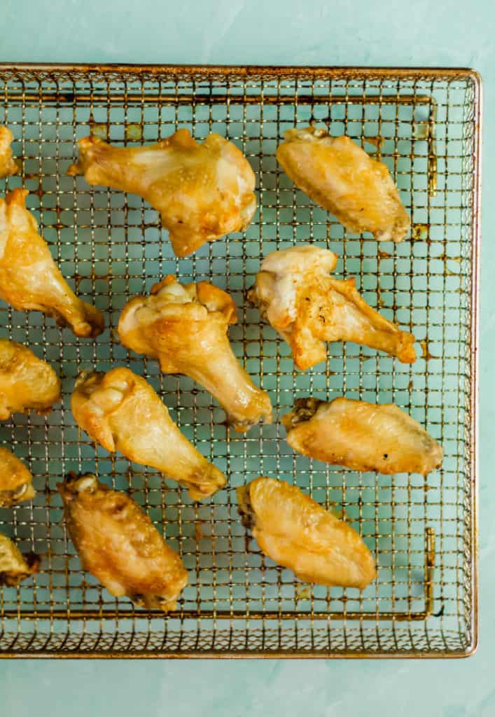 cooked chicken wings in an air fryer basket on a blue background