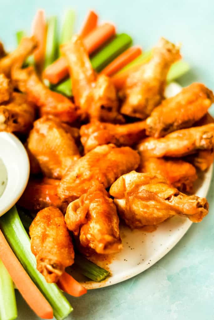 extra crispy air fryer chicken wings piled on a white plate with carrot and celery sticks with a blue background