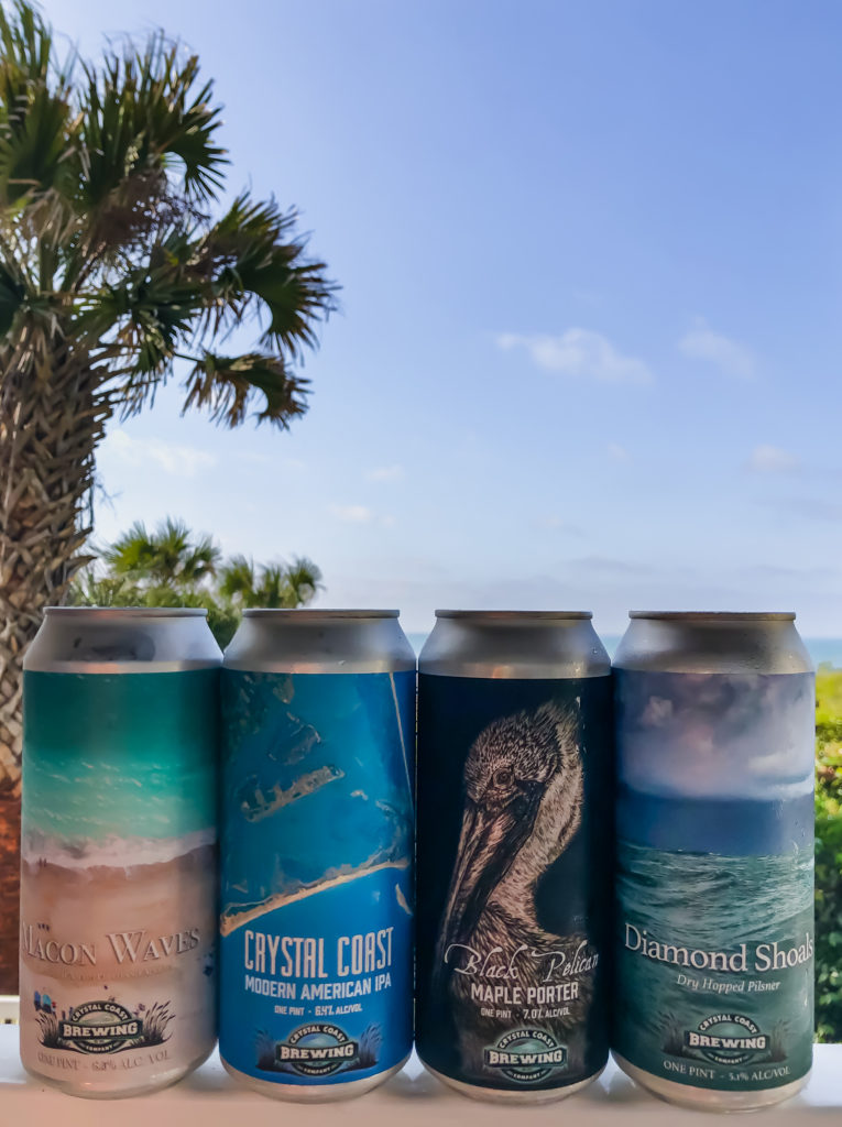 four cans from Crystal Coast Brewing with a palm tree in the background