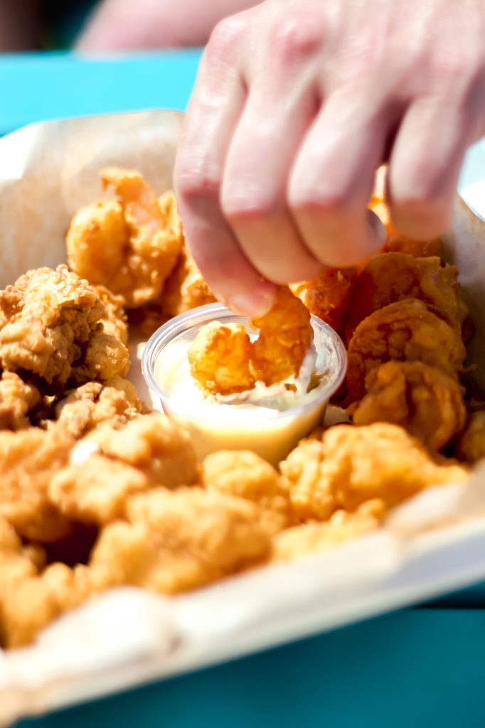 basket of fried seafood with someone dipping a fried shrimp into tarter sauce