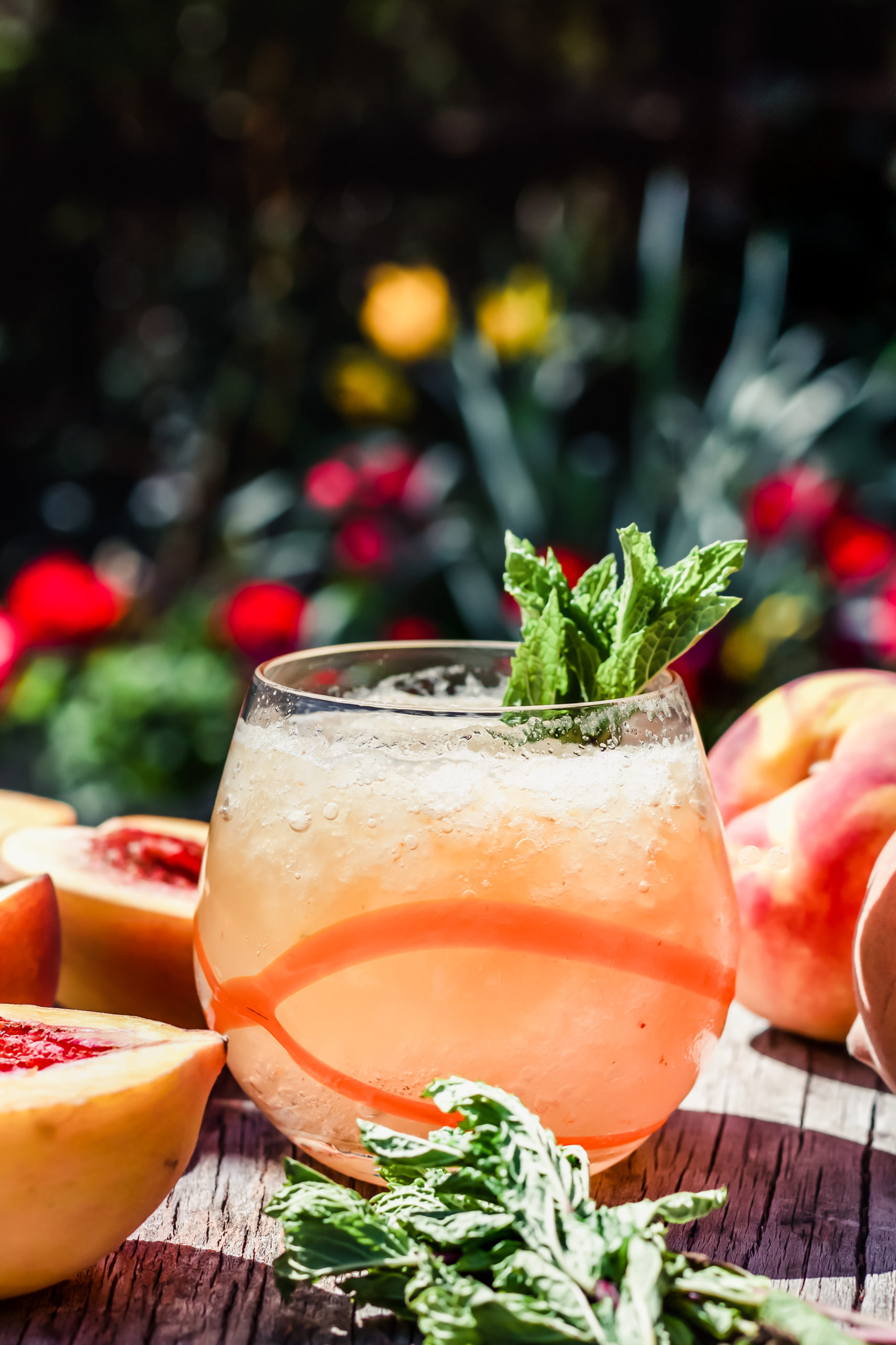 cocktail class with orange detail filled with peach whiskey smash cocktail on a table with flowers in the background