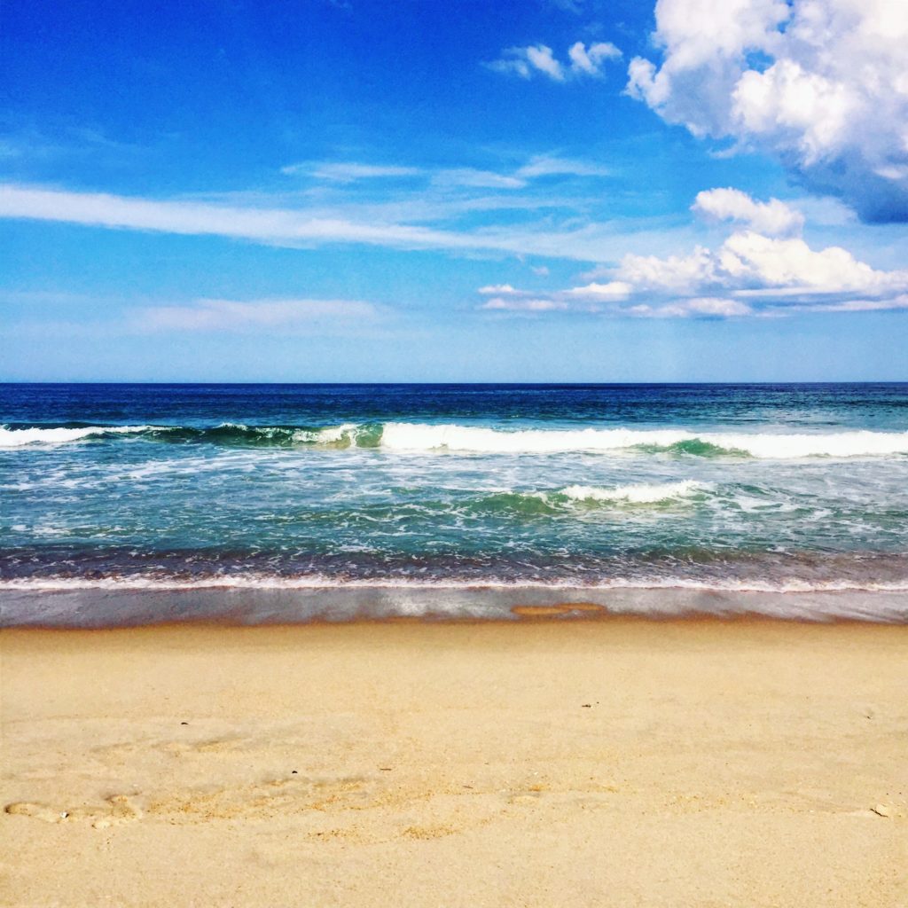 wave breaking on the shore with a bright blue sky and sandy beach