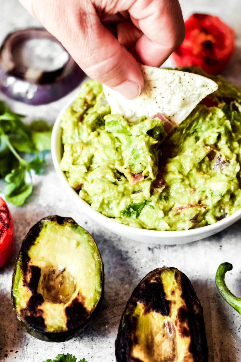 dipping a chip into a whie bowl of vegan guacamole