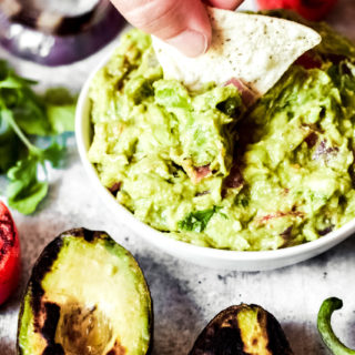 dipping a chip into a whie bowl of vegan guacamole