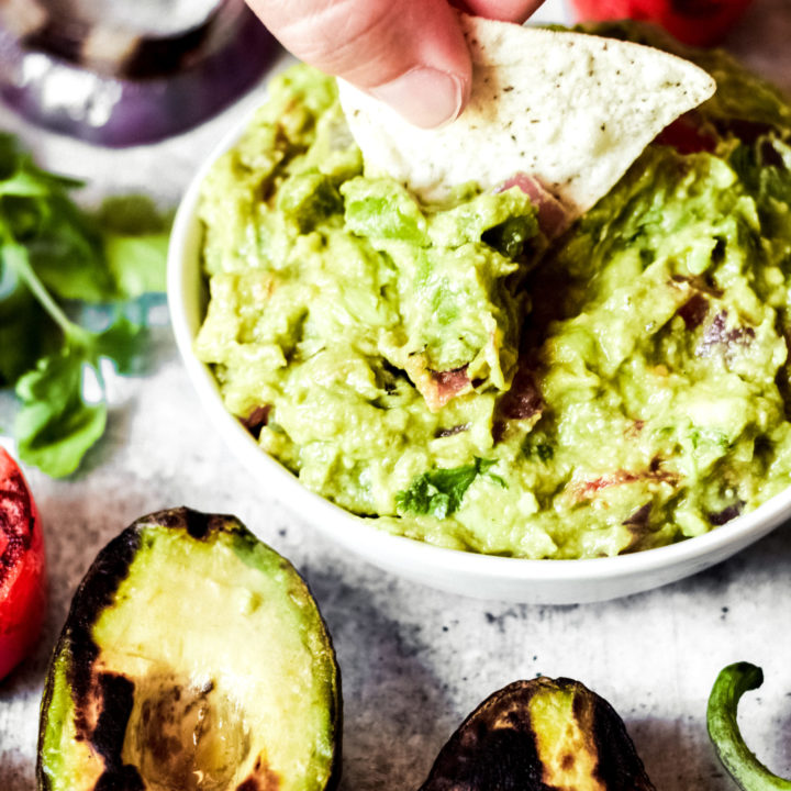 dipping a chip into a whie bowl of vegan guacamole